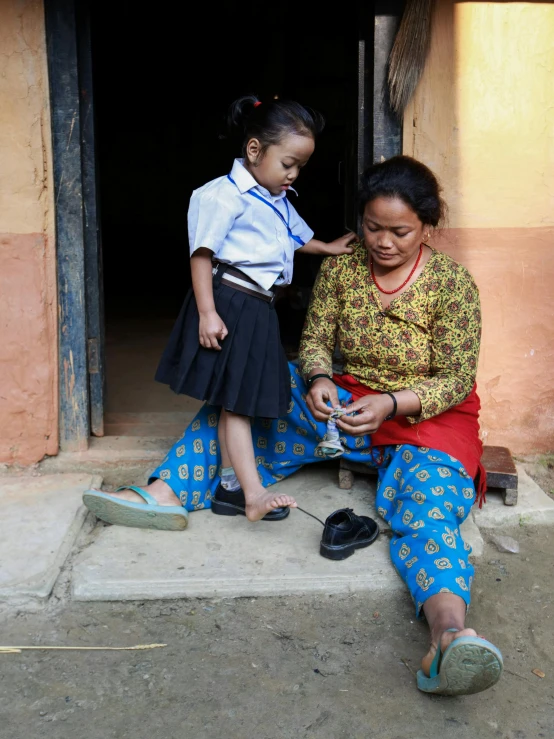 a woman sitting on the ground next to a little girl, silk shoes, nivanh chanthara, slide show, maintenance photo