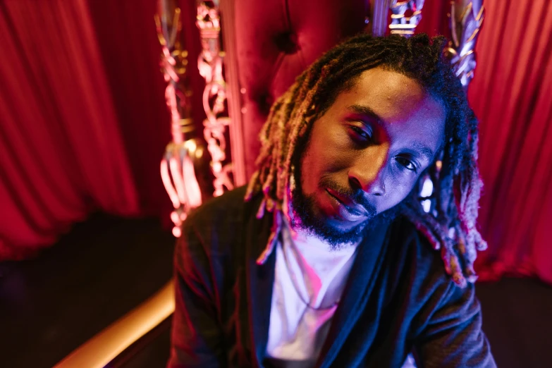 a man with dreadlocks sitting in front of a red curtain, in a nightclub, profile image, ashteroth, portrait image