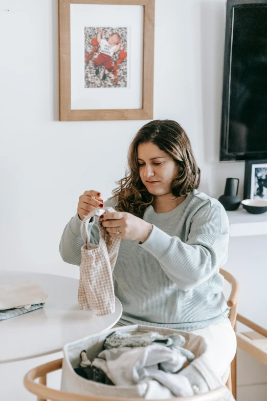 a woman sitting at a table with a bag of clothes, a cross stitch, pexels contest winner, happening, product design shot, sculpting, profile image, at home