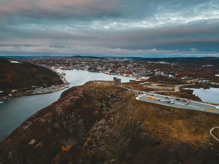 a large body of water sitting next to a lush green hillside, by Jesper Knudsen, pexels contest winner, happening, drone view of a city, moody evening light, stålenhag, harbour