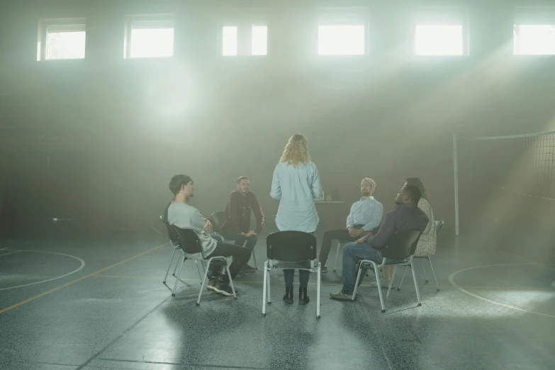 a group of people sitting around a table, in the middle of an empty room, hypnosis, dark hazy room, promo image