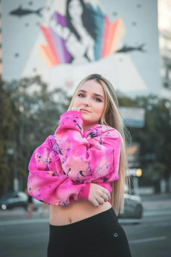 a woman standing in the middle of a street, an album cover, by Julia Pishtar, instagram, happening, wearing a pink hoodie, tie-dye, discord profile picture, midriff