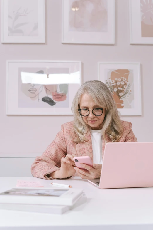 a woman sitting at a table with a laptop and cell phone, a picture, trending on pexels, computer art, white-haired, pastel pink, professional profile picture, wearing square glasses