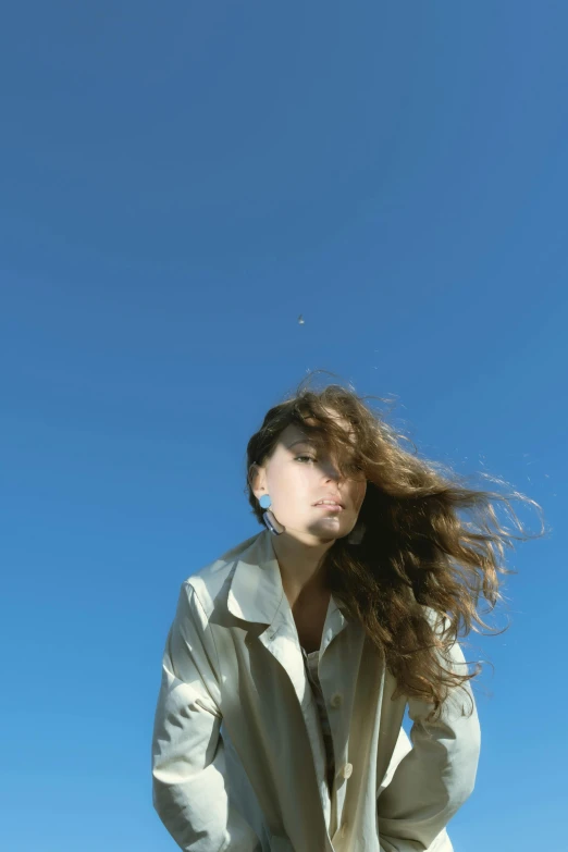 a woman standing on top of a lush green field, an album cover, unsplash, happening, with brown hair, clear blue sky, high winds, ((portrait))