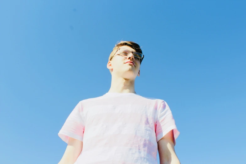 a young man standing in front of a blue sky, an album cover, unsplash, pink shirt, john egbert, very very very pale skin, brightly lit