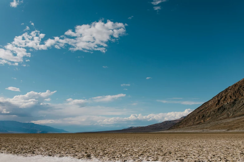 a body of water sitting in the middle of a desert, standing in front of a mountain, death valley, blue sky and white clouds, ash thorp