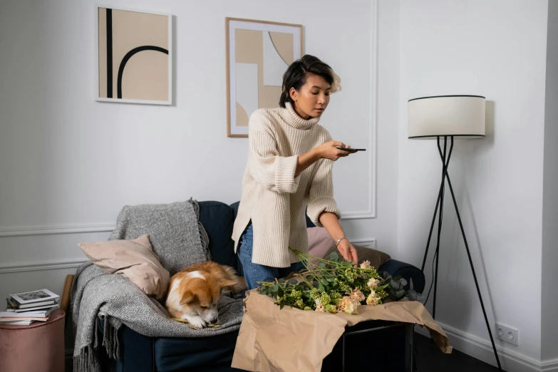 a woman standing in a living room next to a couch, by Julia Pishtar, pexels contest winner, picking up a flower, items and gadget, pets, cardboard