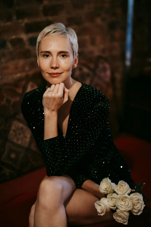 a woman sitting on a red couch holding a bouquet, short platinum hair tomboy, wearing a dress made of stars, kirsi salonen, black dress : : symmetrical face