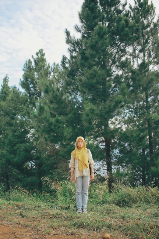 a woman standing in a field with trees in the background, by Basuki Abdullah, unsplash, hurufiyya, yellow and olive color scheme, single pine, movie filmstill, scanned