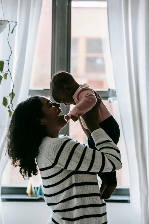 a woman holding a baby in front of a window, fatherly, varying ethnicities, top selection on unsplash, large tall