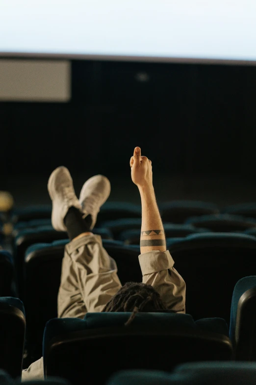 a person laying on a chair in front of a projector screen, inspired by Elsa Bleda, trending on pexels, realism, waving arms, high soles, sitting in a movie theater, with index finger