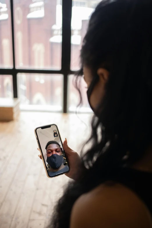a woman taking a picture of herself on her phone, partially masked, photo of a black woman, facing away from camera, mobile learning app prototype