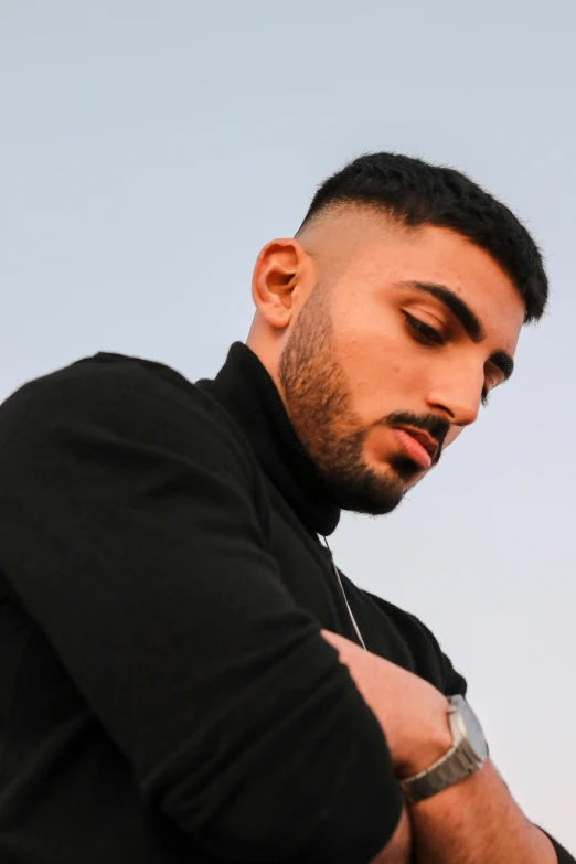 a man in a black shirt standing with his arms crossed, an album cover, inspired by Amir Zand, trending on pexels, hurufiyya, middle eastern skin, lily frank, headshot profile picture, sundown