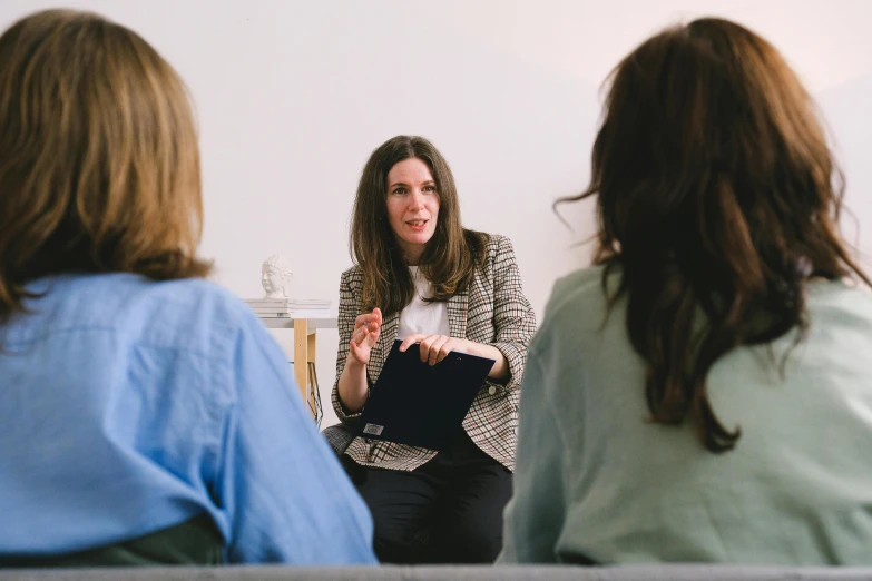 two women sitting on a couch talking to each other, unsplash, three women, robed figures sat around a table, professional photo, person in foreground