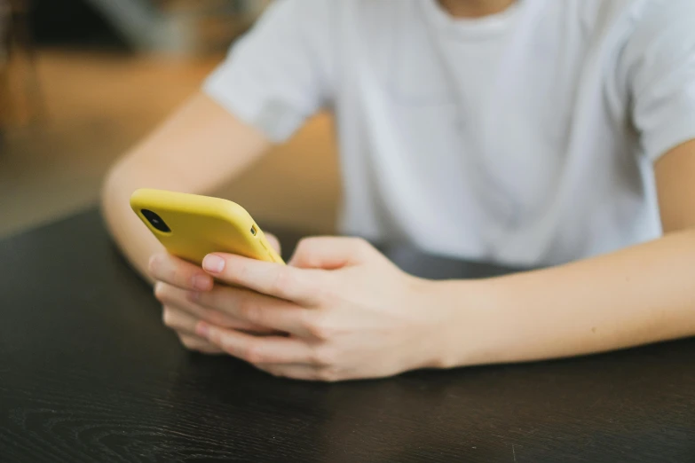 a person sitting at a table with a cell phone, trending on pexels, yellow clothes, aged 13, square, round-cropped