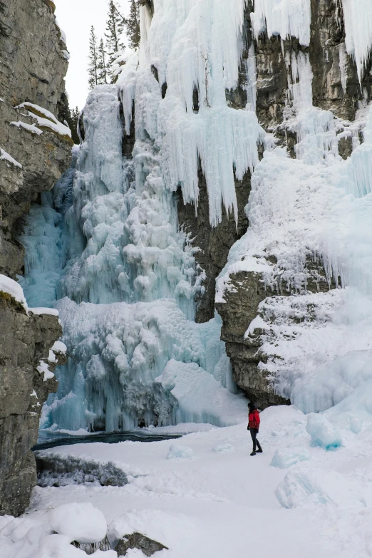 a person standing in front of a frozen waterfall, banff national park, rock formations, february)