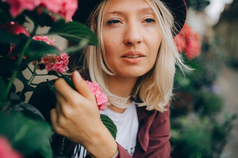 a woman standing in front of a bunch of flowers, a photo, by Julia Pishtar, pexels contest winner, close up of a blonde woman, woman in streetwear, rosy cheeks, gardening