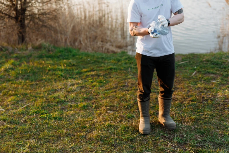 a man standing next to a body of water, wearing boots, water to waste, dressed in a white t shirt, avatar image