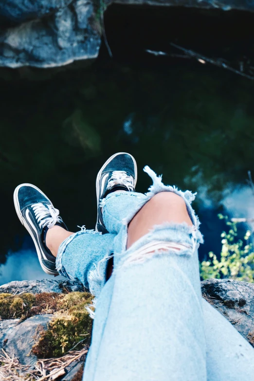 a person sitting on top of a rock next to a body of water, trending on pexels, happening, blue jeans and grey sneakers, metallic reflective, teenage girl, ripped clothing