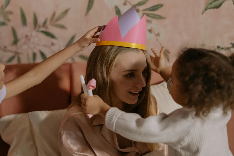 a woman putting a crown on a little girl, a cartoon, by Emma Andijewska, pexels contest winner, happening, photoshoot for skincare brand, party hats, holding wand, still from film