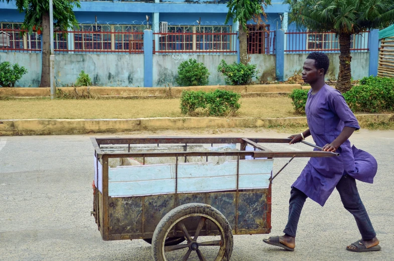 a man walking down a street with a cart, by Chinwe Chukwuogo-Roy, pexels contest winner, visual art, school class, biological photo, coloured, government archive photograph