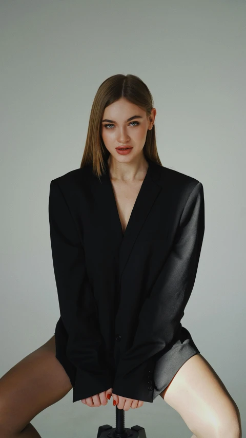 a woman sitting on a chair posing for a picture, by Emma Andijewska, trending on pexels, purism, long black jacket, collar on neck, portrait sophie mudd, tailored clothing