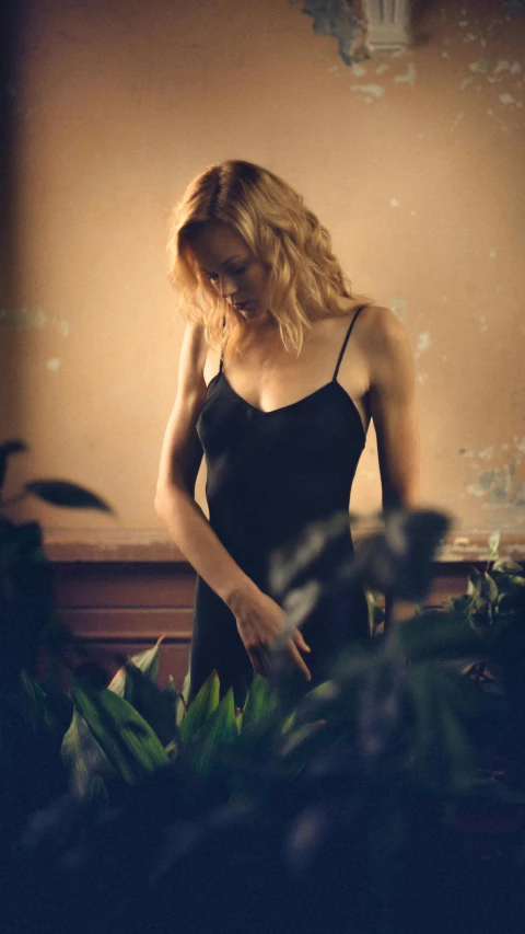 a woman in a black dress standing in front of a window, inspired by Nan Goldin, unsplash, nicole kidman, next to a plant, medium format. soft light, seductive camisole