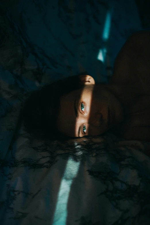 a close up of a person laying on a bed, inspired by Elsa Bleda, unsplash contest winner, surrealism, blue shining eyes, looking up at the camera, middle of the night, gif