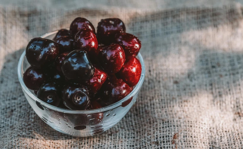 a glass bowl filled with cherries on top of a table, by Emma Andijewska, pexels, jelly - like texture, black forest, made of glazed, ear