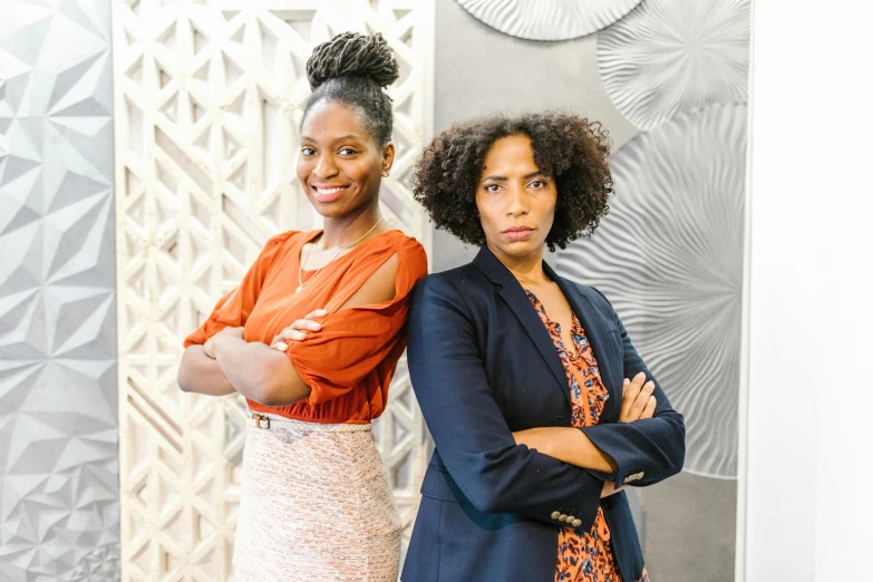 two women standing next to each other in front of a wall, a portrait, pexels, black arts movement, corporate photo, serious business, brown, afro tech