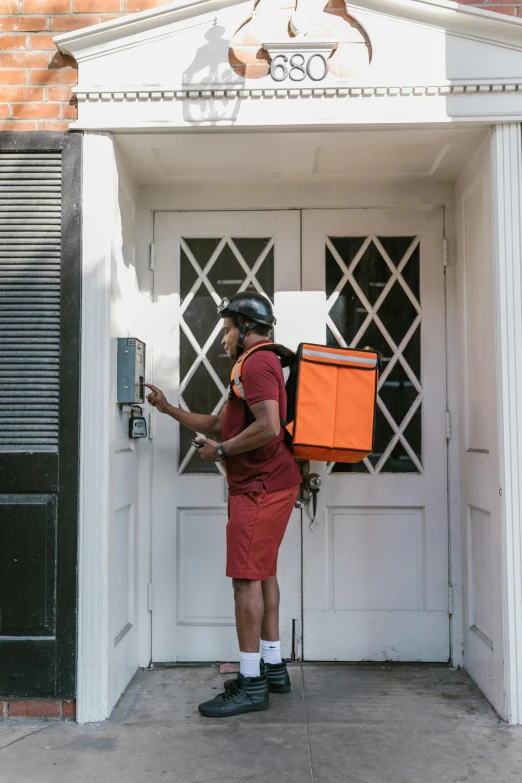 a man that is standing in front of a door, delivering parsel box, orange and black, in louisiana, lightweight