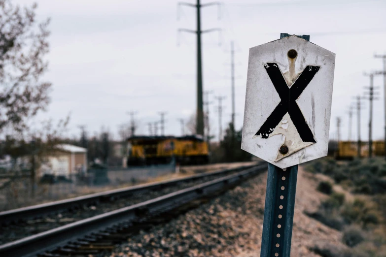 a railroad crossing sign with a train in the background, a portrait, trending on pexels, x logo, forgotten, cross composition, thumbnail