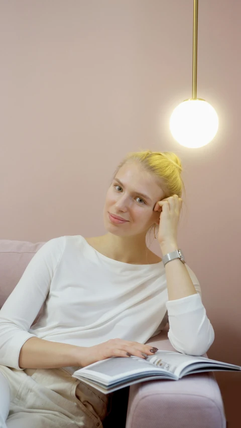 a woman sitting on a couch reading a book, inspired by Louisa Matthíasdóttir, pexels, minimalism, very very pale blond hair, lovingly looking at camera, girl with a pearl earringl, sitting in a waiting room