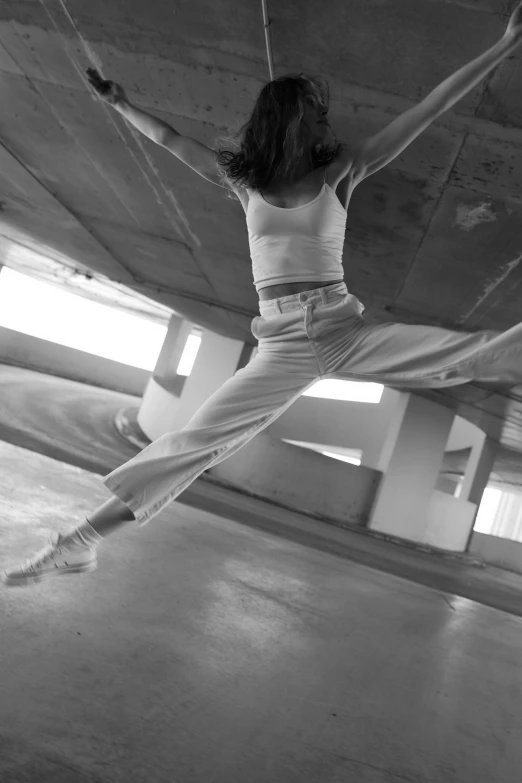 a woman that is jumping in the air, a black and white photo, inspired by Alexander Rodchenko, pexels contest winner, arabesque, white pants, under bridge, breakdancing, detail