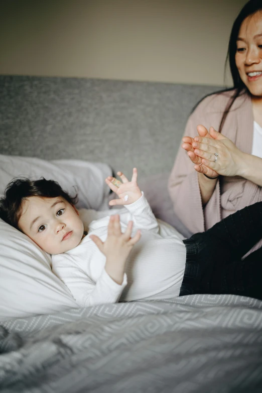 a woman sitting on top of a bed next to a baby, pexels, waving hands, happily tired, holding hands, soft vinyl