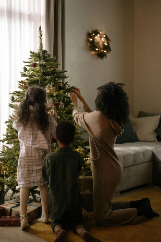 a woman and two children decorating a christmas tree, by Andries Stock, pexels contest winner, cozy environment, gif, subtle detailing, black fir