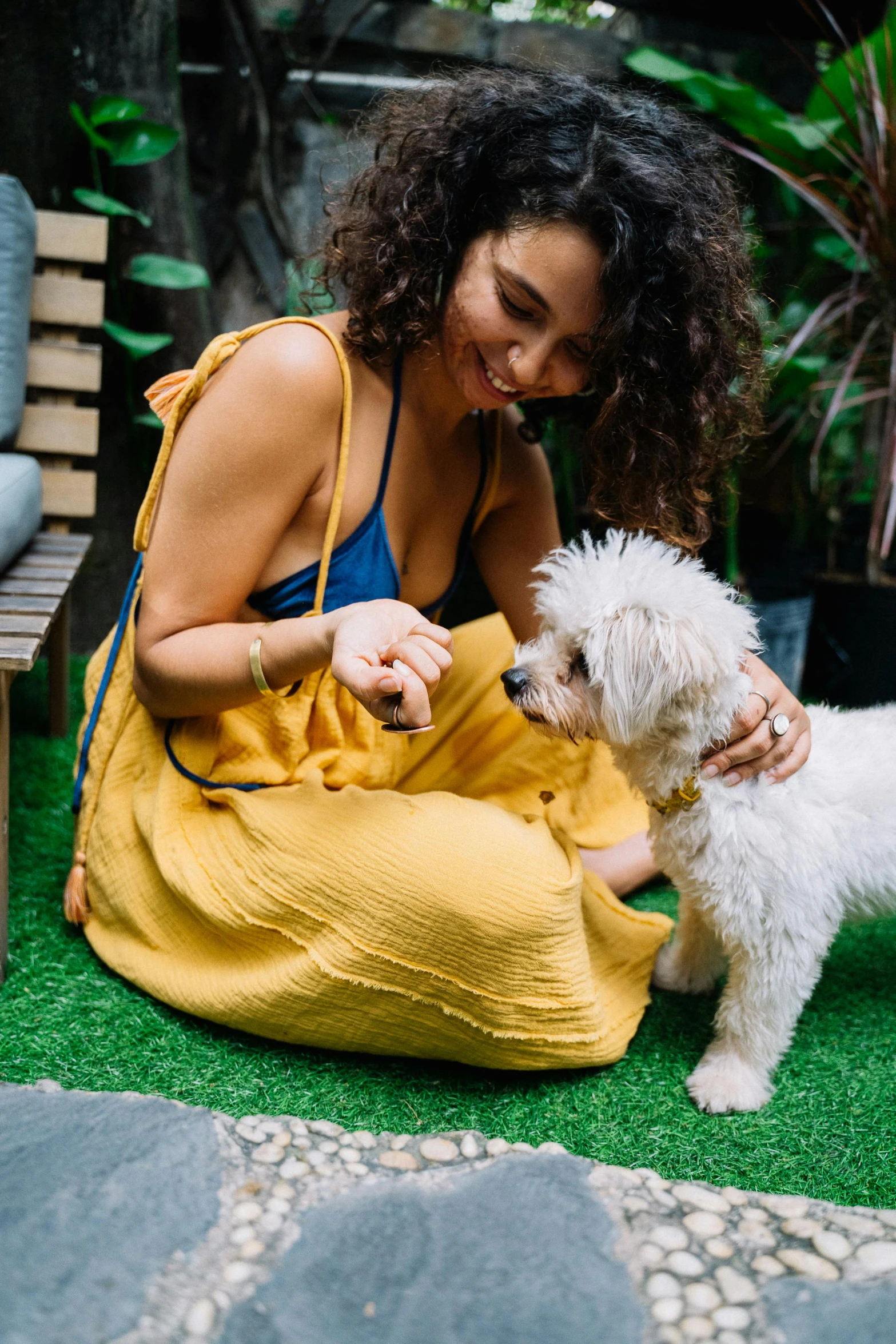 a woman in a yellow dress petting a white dog, trending on unsplash, happening, curly haired, sitting in the garden, small dog, in sao paulo