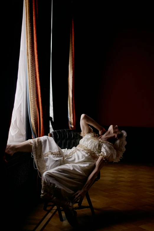 a woman sitting in a chair in front of a window, inspired by Karl Bryullov, pexels contest winner, baroque, hanging upside down, draped in silky gold, dim studio lighting, swings