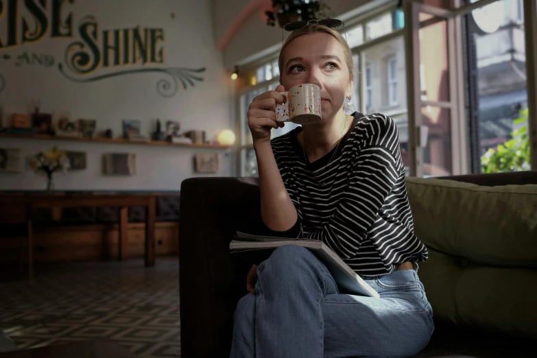 a woman sitting on a couch drinking a cup of coffee, inspired by Jakob Häne, shine, coffee shop, local illumination, filmstill
