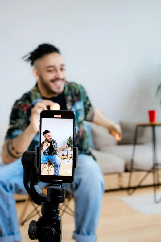 a man sitting on a chair holding a cell phone, a picture, trending on pexels, video camera, two still figures facing camera, playful composition, lgbtq