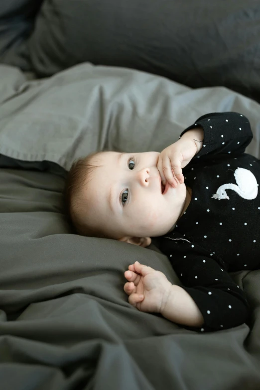 a baby laying on top of a bed next to a pillow, a portrait, unsplash, black dots, long sleeves, on black background, duck