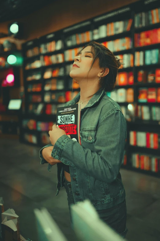 a woman standing in front of a bookshelf holding a book, an album cover, pexels contest winner, in a mall, relaxed pose, dazzling lights, androgynous person