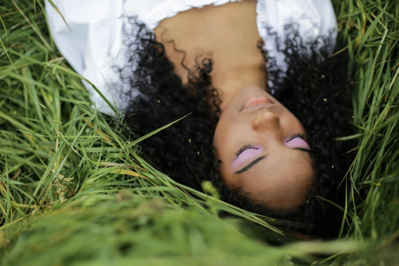 a woman laying in the grass with her eyes closed, pexels contest winner, renaissance, black curly hair, natural complexion, promo image, seen from below