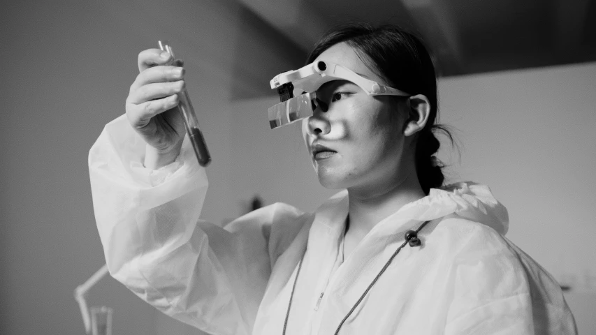 a black and white photo of a woman in a lab coat, a black and white photo, by Emma Andijewska, unsplash, bauhaus, goggles on forehead, jingna zhang, art student, performance