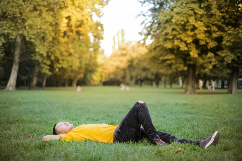 a man laying on top of a lush green field, by Julia Pishtar, pexels, realism, wearing a modern yellow tshirt, in a park, sleeping, during autumn