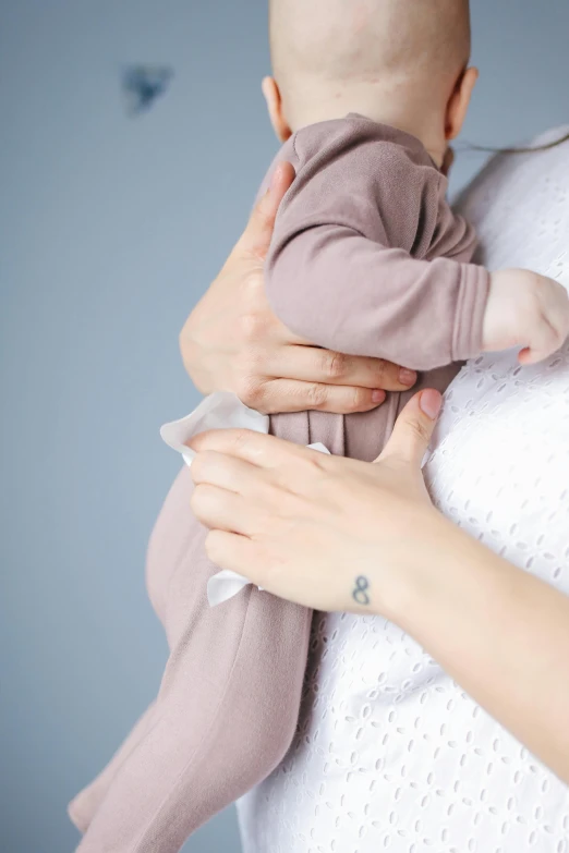 a woman holding a baby in her arms, shutterstock, symbolism, touching her clothes, soft colours, grey, plain background