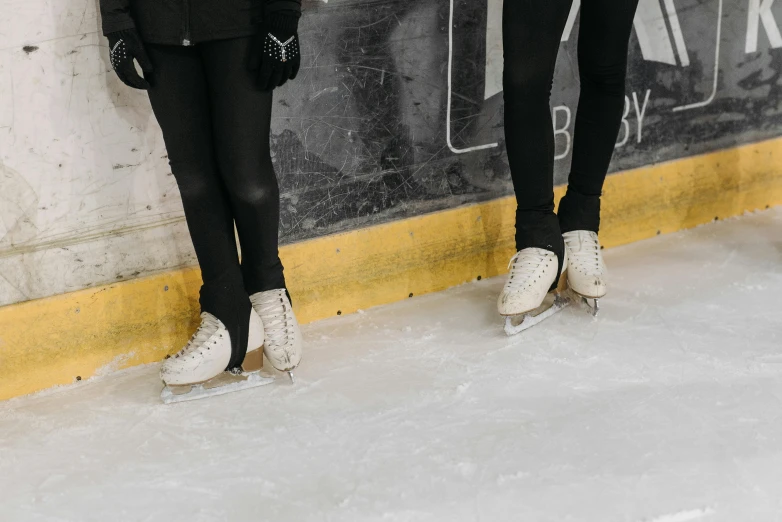 a couple of women standing next to each other on a ice rink, trending on pexels, black and silver, bottom angle, soft white rubber, normal legs