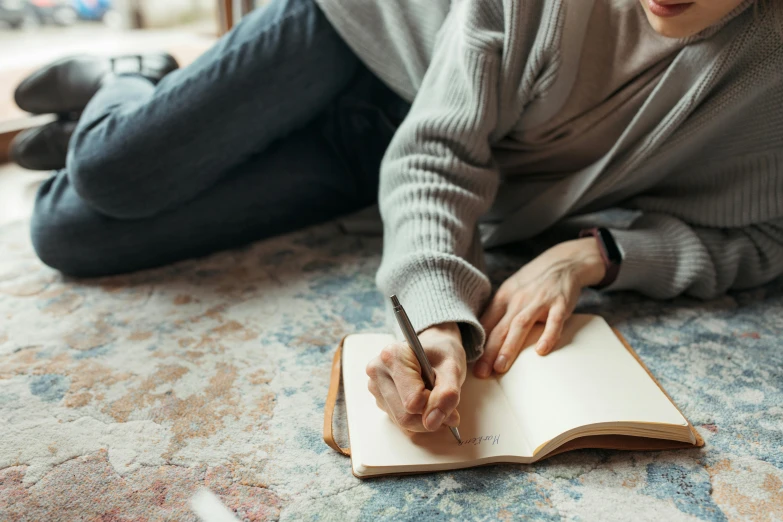 a woman sitting on the floor writing on a notebook, trending on pexels, visual art, fan favorite, background image, androgynous person, no watermark