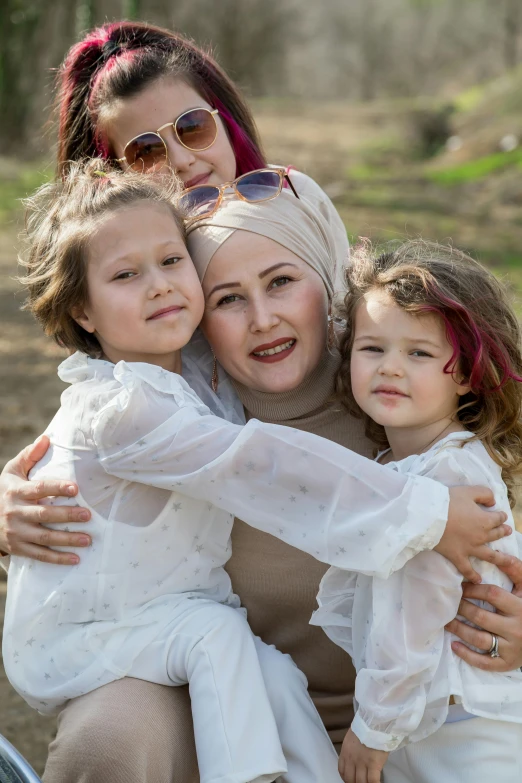 a woman sitting on a bench with two little girls, by Maryam Hashemi, shutterstock, portrait of women embracing, wearing a turban, 15081959 21121991 01012000 4k, of a family standing in a park