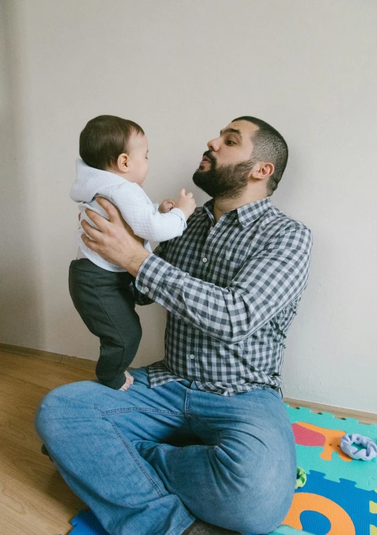 a man sitting on the floor holding a baby, pexels contest winner, assyrian, standing upright, forward facing pose, feels good man